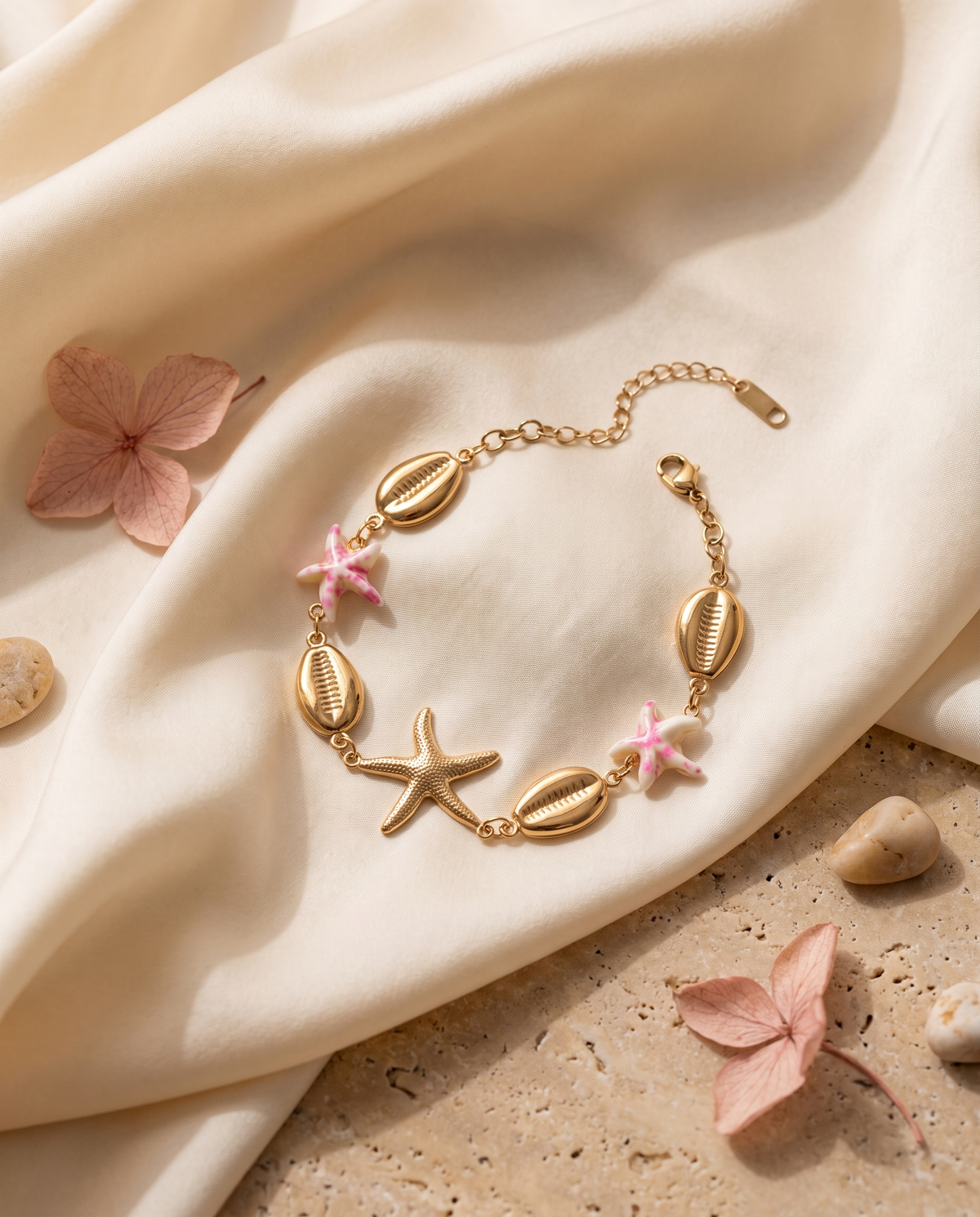 Pulsera dorada con estrella de mar y detalles rosas sobre tejido color crema
